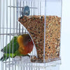 A transparent anti-spill parrot feeder with multiple compartments filled with seeds and a bird inside