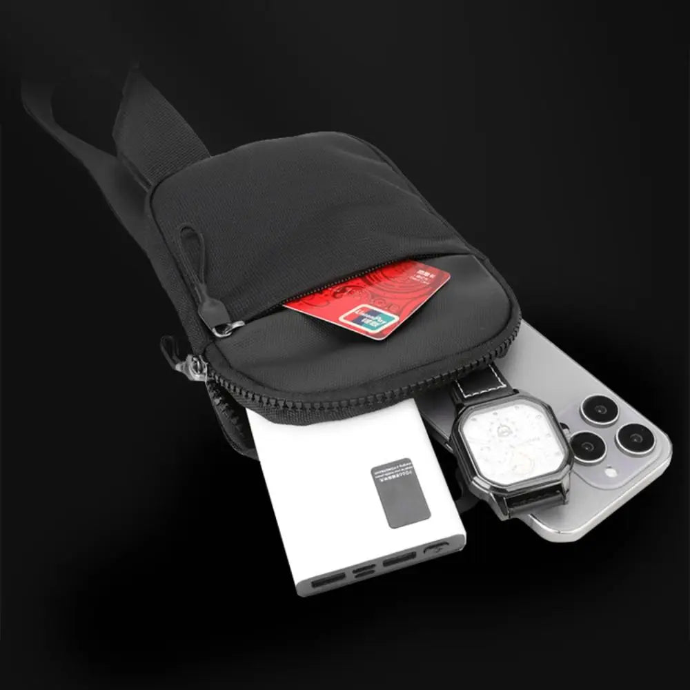 A black canvas crossbody sling bag is shown next to a smartphone and a white power bank.