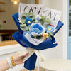 A hand holds a bouquet of handmade crochet artificial blue and white flowers wrapped in sheer paper.