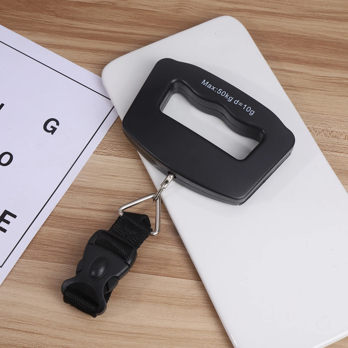 A black portable digital luggage scale is shown resting on a white surface next to a scale measuring tape.
