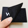 A close-up of a black tactical morale patch with white embroidery and a hook and loop fastener being held by a hand.