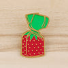A gold-rimmed enamel pin shaped like a strawberry with a green leafy top.
