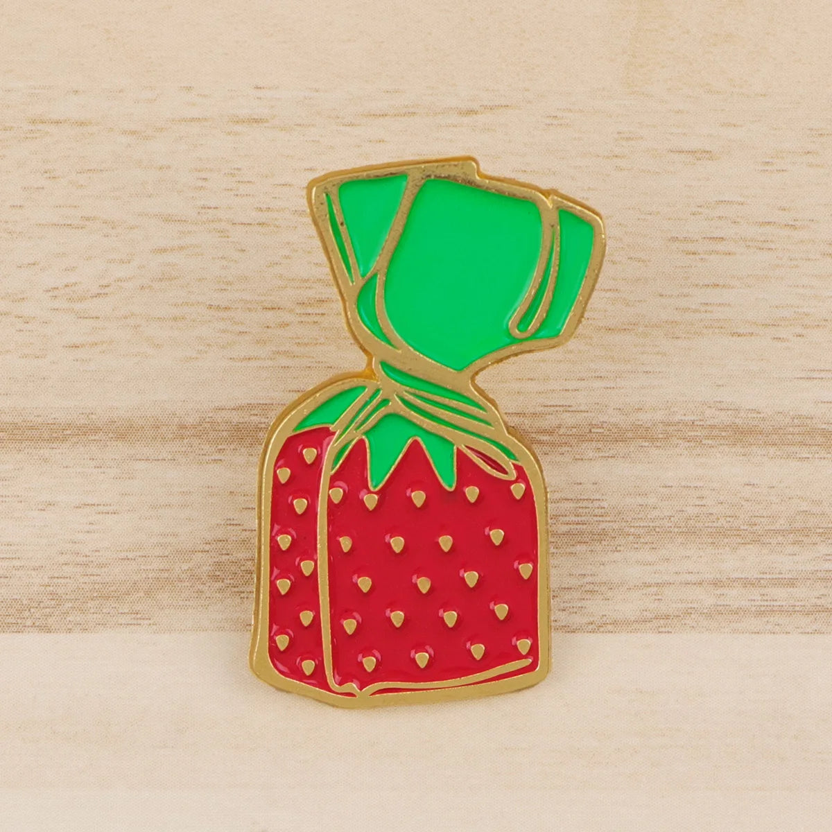 A gold-rimmed enamel pin shaped like a strawberry with a green leafy top.