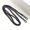 Black metal chain purse strap with a secure buckle lying on a white surface.