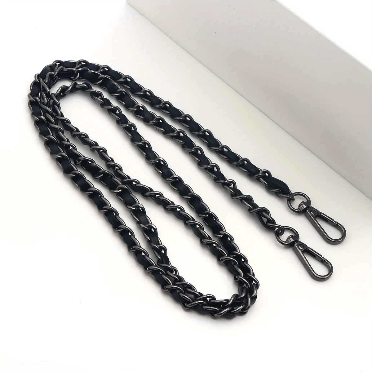 Black metal chain purse strap with a secure buckle lying on a white surface.