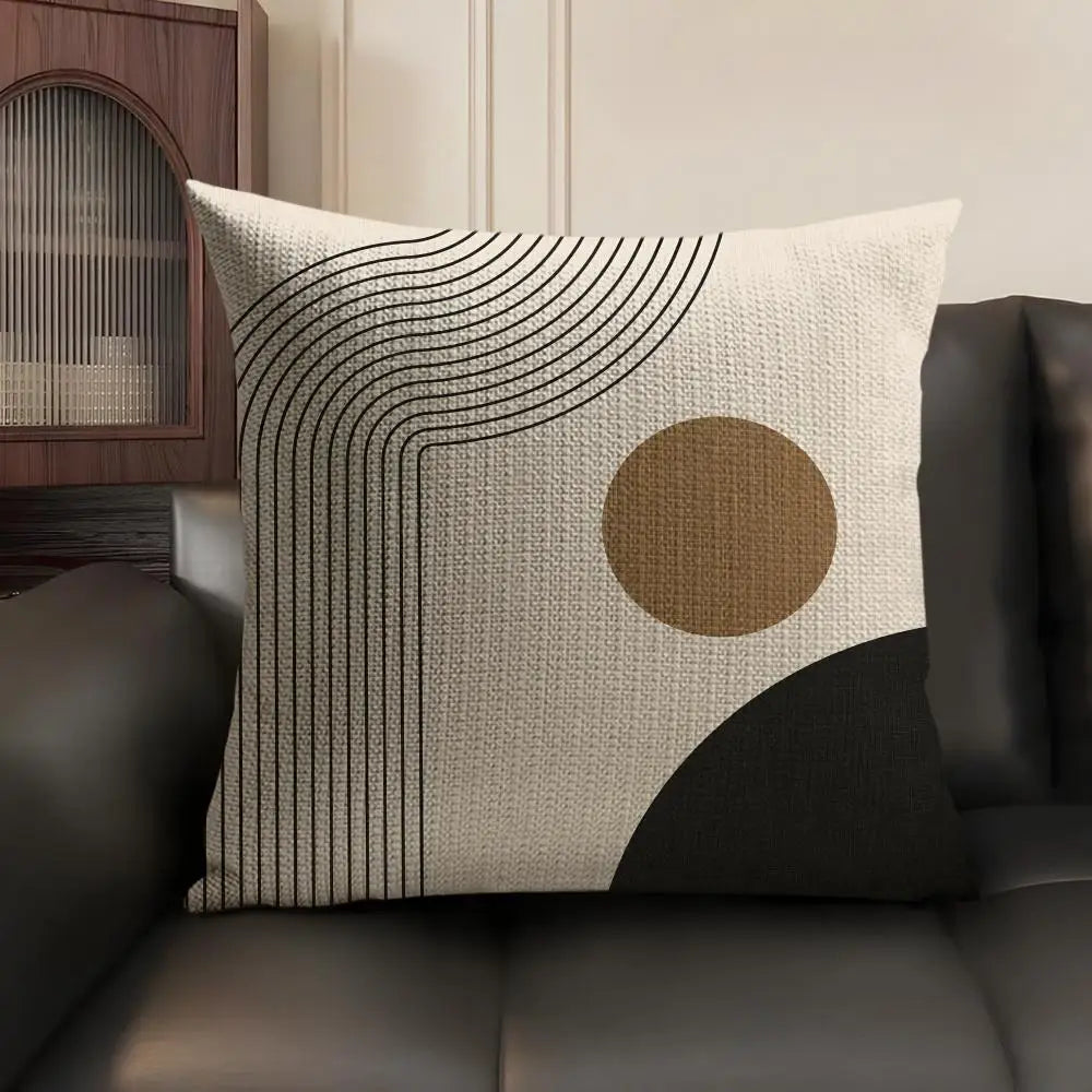 A beige linen cushion cover featuring black geometric lines and a circular tan accent on a dark sofa.