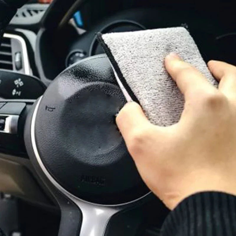 A hand is holding a gray microfiber scrub sponge, preparing to clean a car interior surface.