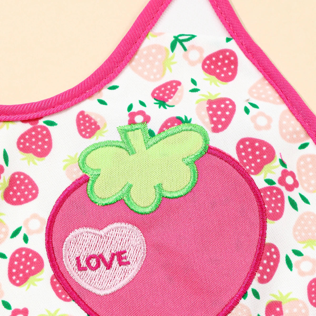 A pink and white baby bib featuring a heart design and strawberry prints.