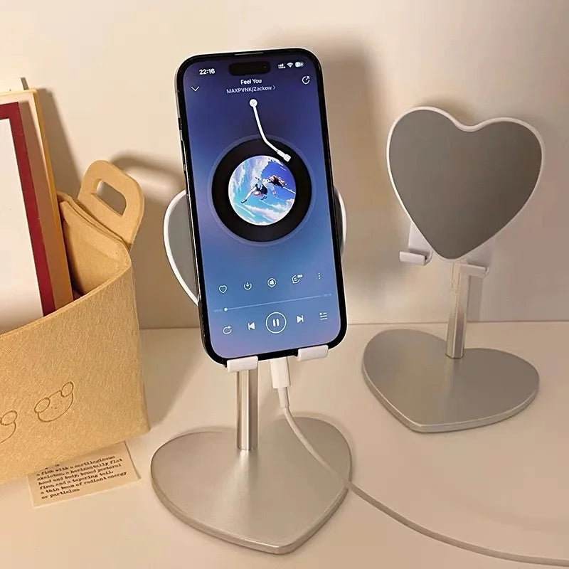 A silver adjustable heart-shaped stand holding a smartphone displaying a music app interface.