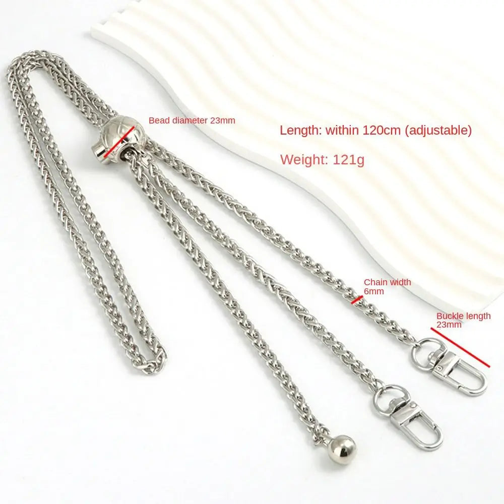 Silver metal chain strap with a bead and buckle, shown next to a cream-colored leather item.