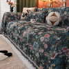 A dark floral jacquard sofa blanket featuring pink and green flowers and decorative tassels on a bed.