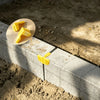 Two yellow masonry line corner clips with anti-slip locks are placed on a concrete block.