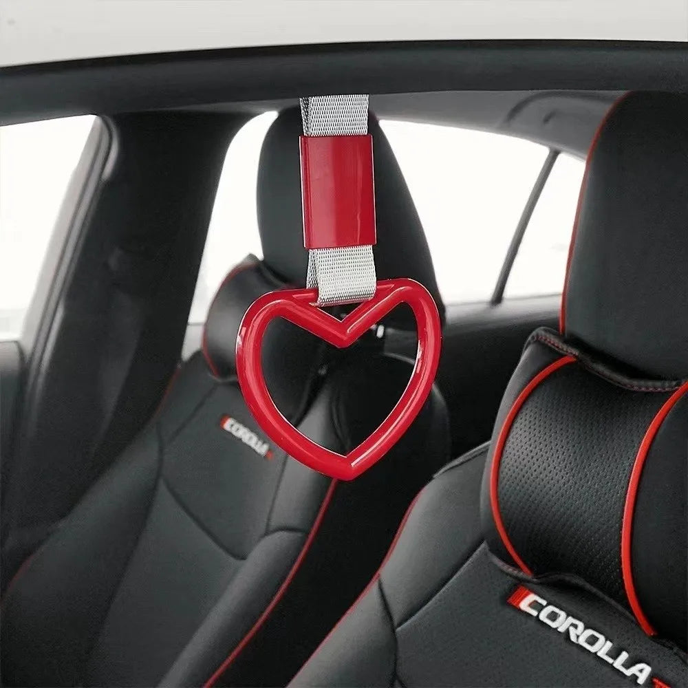 Red heart-shaped car handle decor with a holographic strap hanging from the interior of a car seat.