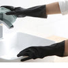 A hand wearing a black rubber cleaning glove is shown gripping a faucet in a white sink.