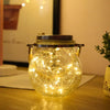 A glass solar lantern with a warm ambient glow sits on a wooden surface.