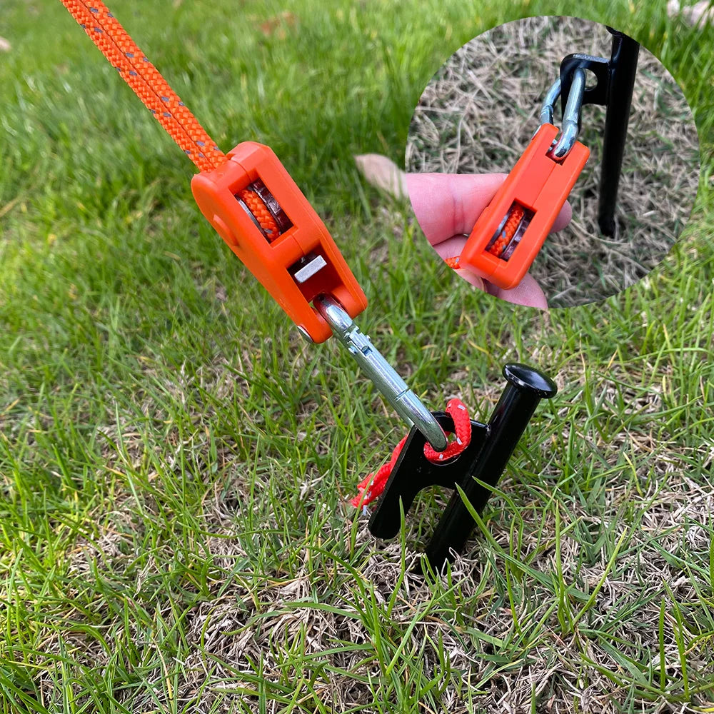 Orange camping rope tensioners with pulley buckles are shown lying on green grass.
