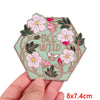 A pink and green floral embroidery patch featuring a bee and wild flowers on a light green fabric background.