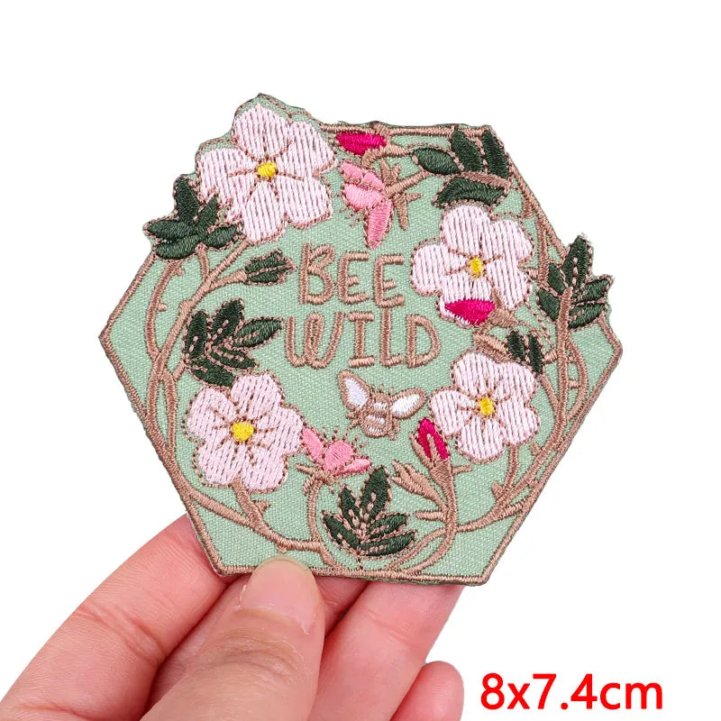 A pink and green floral embroidery patch featuring a bee and wild flowers on a light green fabric background.