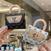 A hand holds a mini floral textured crossbody tote bag with light beige leather and gold chain in a modern indoor setting.