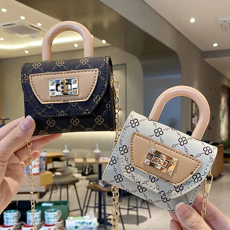 A hand holds a mini floral textured crossbody tote bag with light beige leather and gold chain in a modern indoor setting.