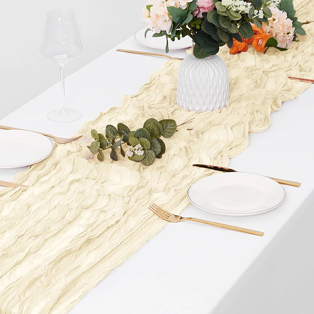 A white table setting featuring a beige semi-sheer gauze table runner, plates, silverware, and floral arrangement.