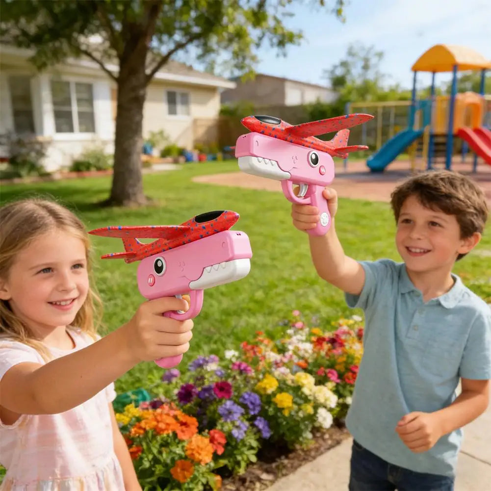A young girl and boy are playing with pink foam catapult airplane toys outdoors in a garden setting.