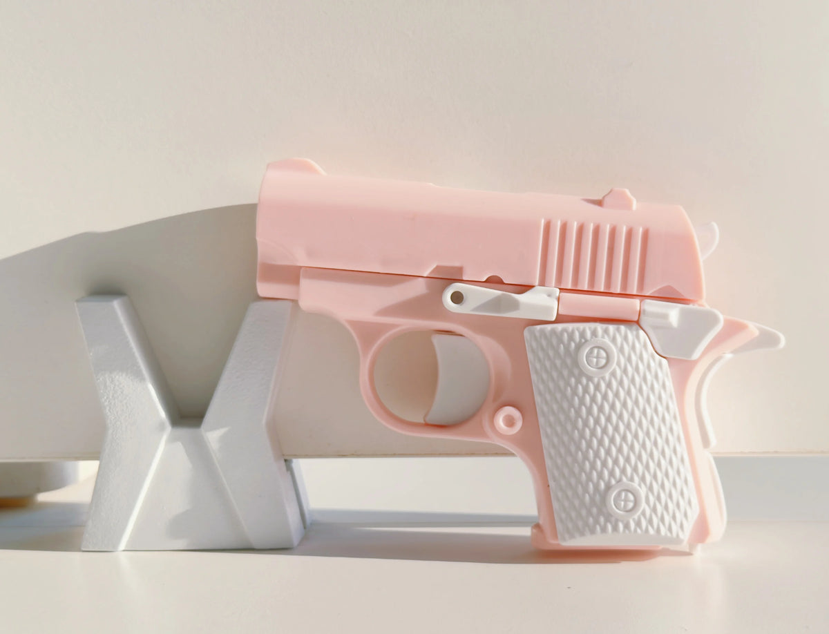A pink mini 3D printed gravity fidget pistol toy resting on a white surface.