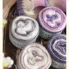 Rolls of soft, colorful wool-blend yarn in shades of pink and purple for knitting and crochet projects.