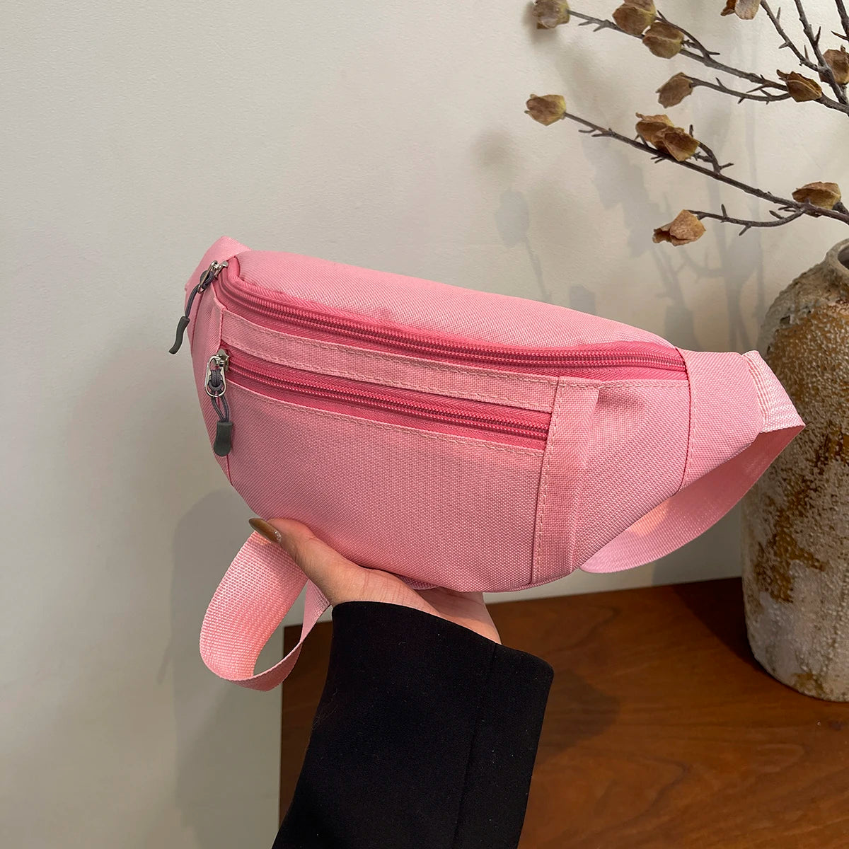 A hand holds a pink nylon crossbody waist pack against a white background.