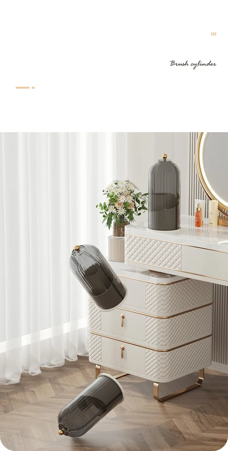 A white and gold rotating makeup brush holder with a dark gray dustproof lid displayed on a vanity table.