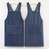 A pair of navy blue striped denim cross-back aprons displayed on a hanger.