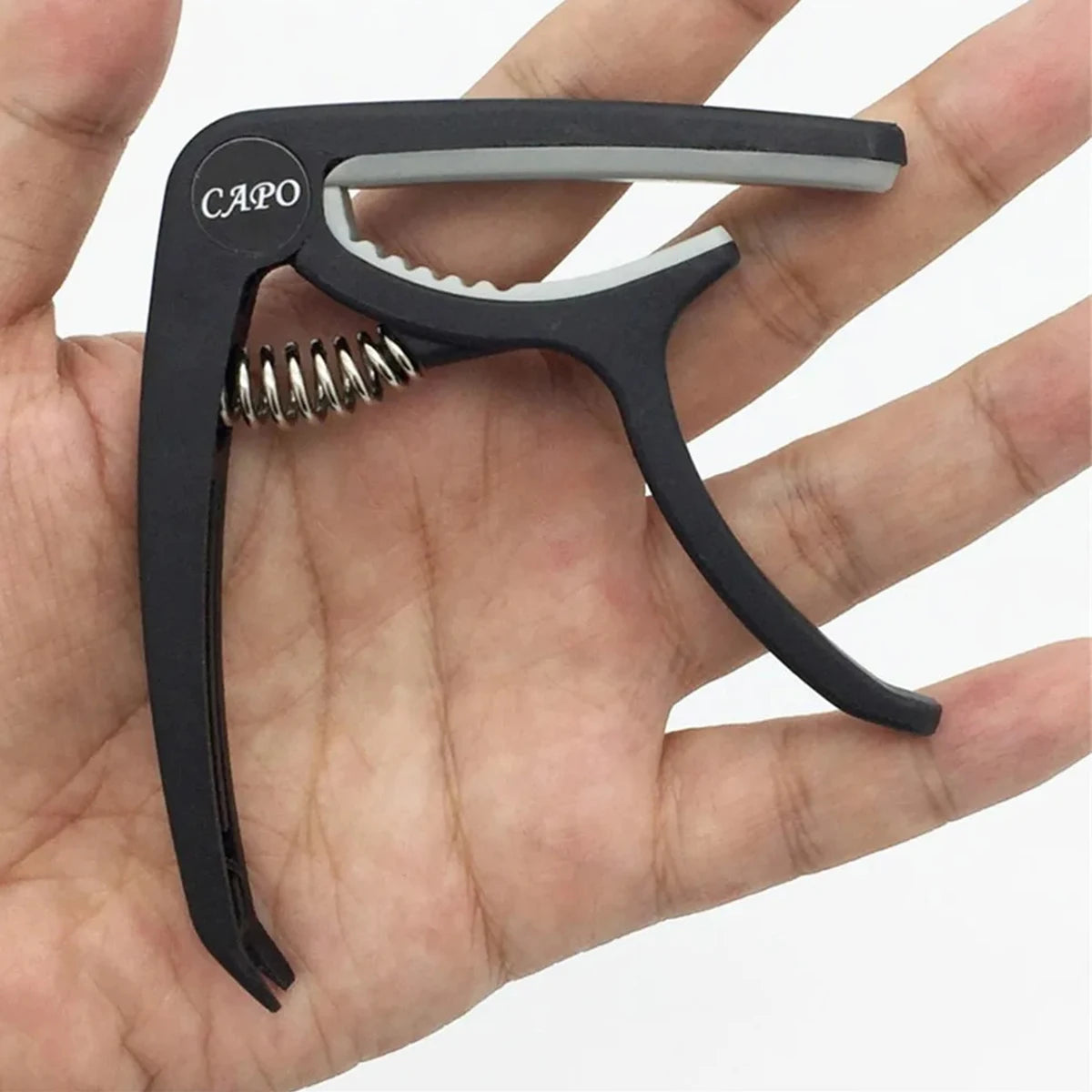A black capo is shown being held by a hand, demonstrating the accessory for guitar playing.