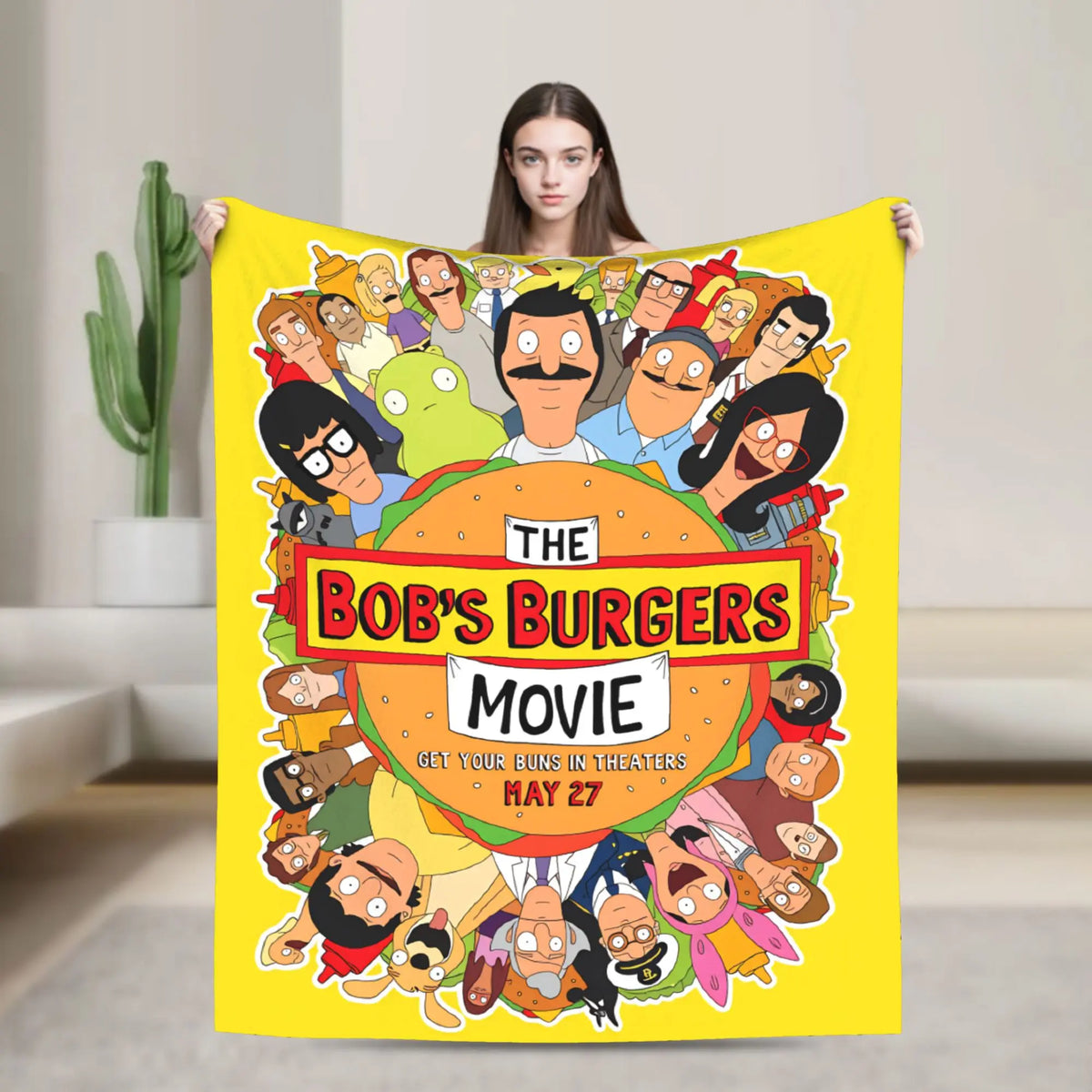 A yellow throw blanket featuring a cartoon illustration of characters from The Bob's Burgers movie poster.