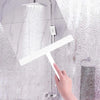 A hand is using a white soft silicone shower squeegee with a hanging hook to clean glass shower walls.
