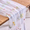 Sheer white tulle table runner featuring delicate floral embroidery on a wooden table.
