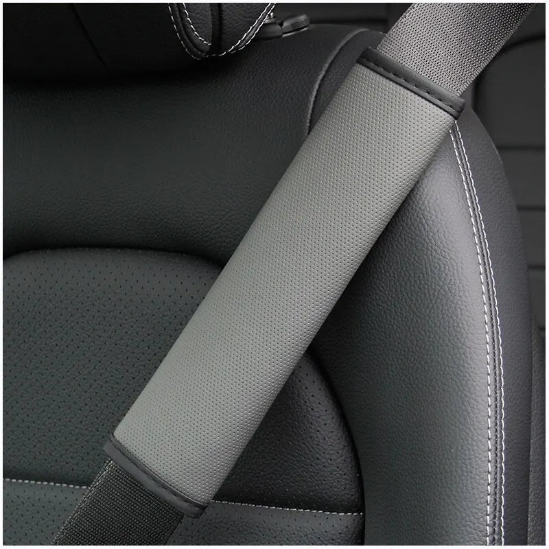 A gray PU leather embossed seat belt shoulder cushion is shown on a dark automotive seat.
