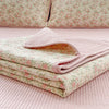 Pink floral quilted coverlet folded on a pink quilted bedspread.