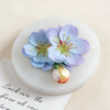 Fleur bleu clair et violette en silicone posée sur une surface blanche.