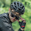 A person wearing a black helmet and sunglasses is looking directly at the camera in an outdoor, green setting.