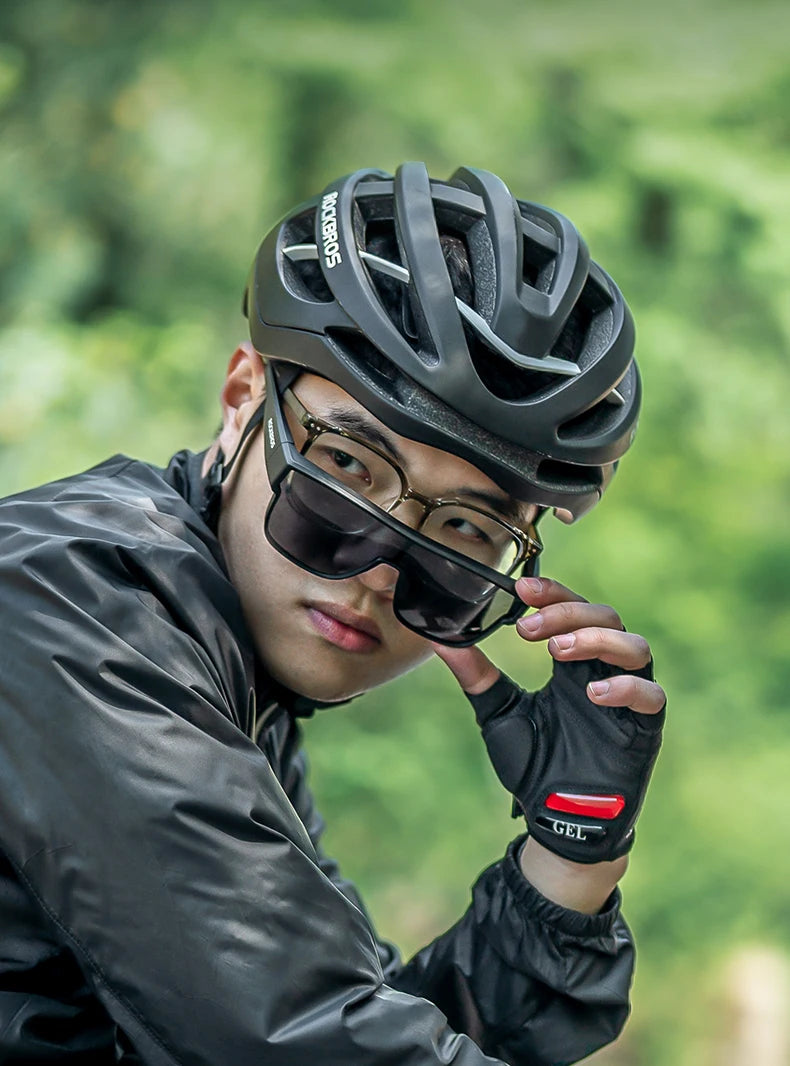 A person wearing a black helmet and sunglasses is looking directly at the camera in an outdoor, green setting.