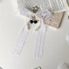 A white lace bow keychain featuring pearl strands and a black heart charm.