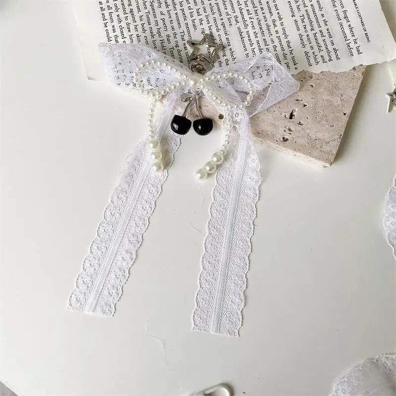 A white lace bow keychain featuring pearl strands and a black heart charm.