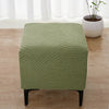 A square ottoman cover in olive green with a geometric, wavy pattern resting on a wooden floor.