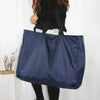 A navy blue reusable large-capacity grocery tote bag is shown hanging against a white background.
