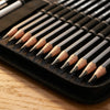 A close-up view of a set of graphite and charcoal pencils arranged in a black zippered case on a wooden surface.