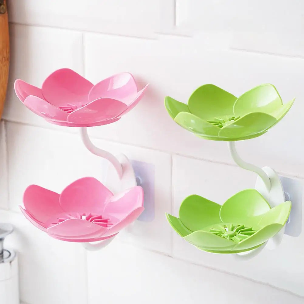 Two pink and green lotus-shaped bathroom storage racks with drainage features mounted on a white tile wall.
