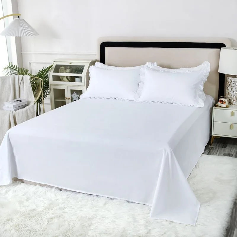 A white bed with a neutral headboard and white ruffled pillow covers on a white duvet, set against a bright interior.