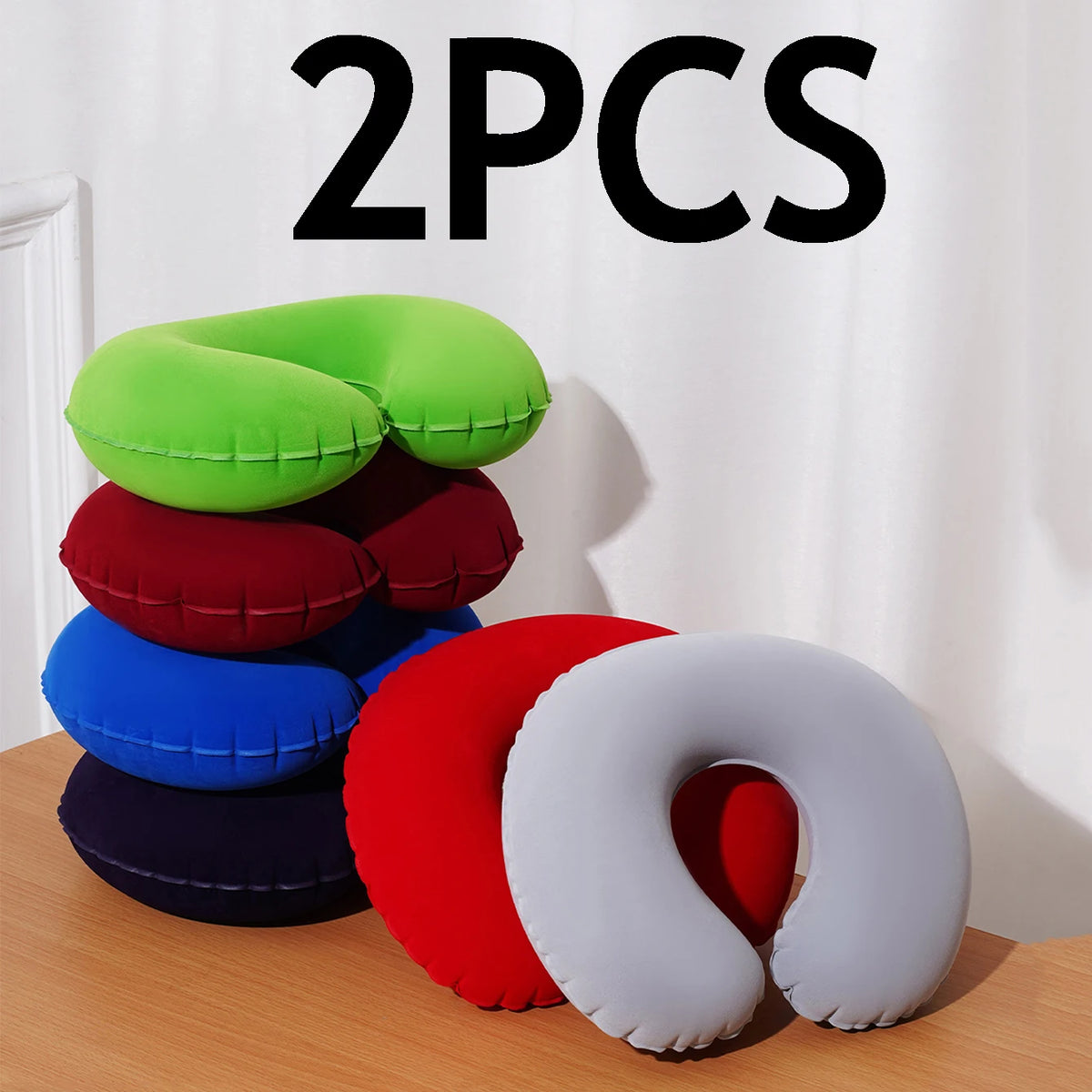 Two green, red, blue, and white inflatable U-shaped travel neck pillows displayed on a wooden surface.