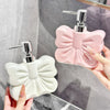 A hand holds two decorative ceramic pump dispensers, one pink and one white, against a gray marble background.