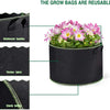 A black grow bag filled with pink and white flowers, showing reinforced handles, thicker fabric, and a sturdy bottom.